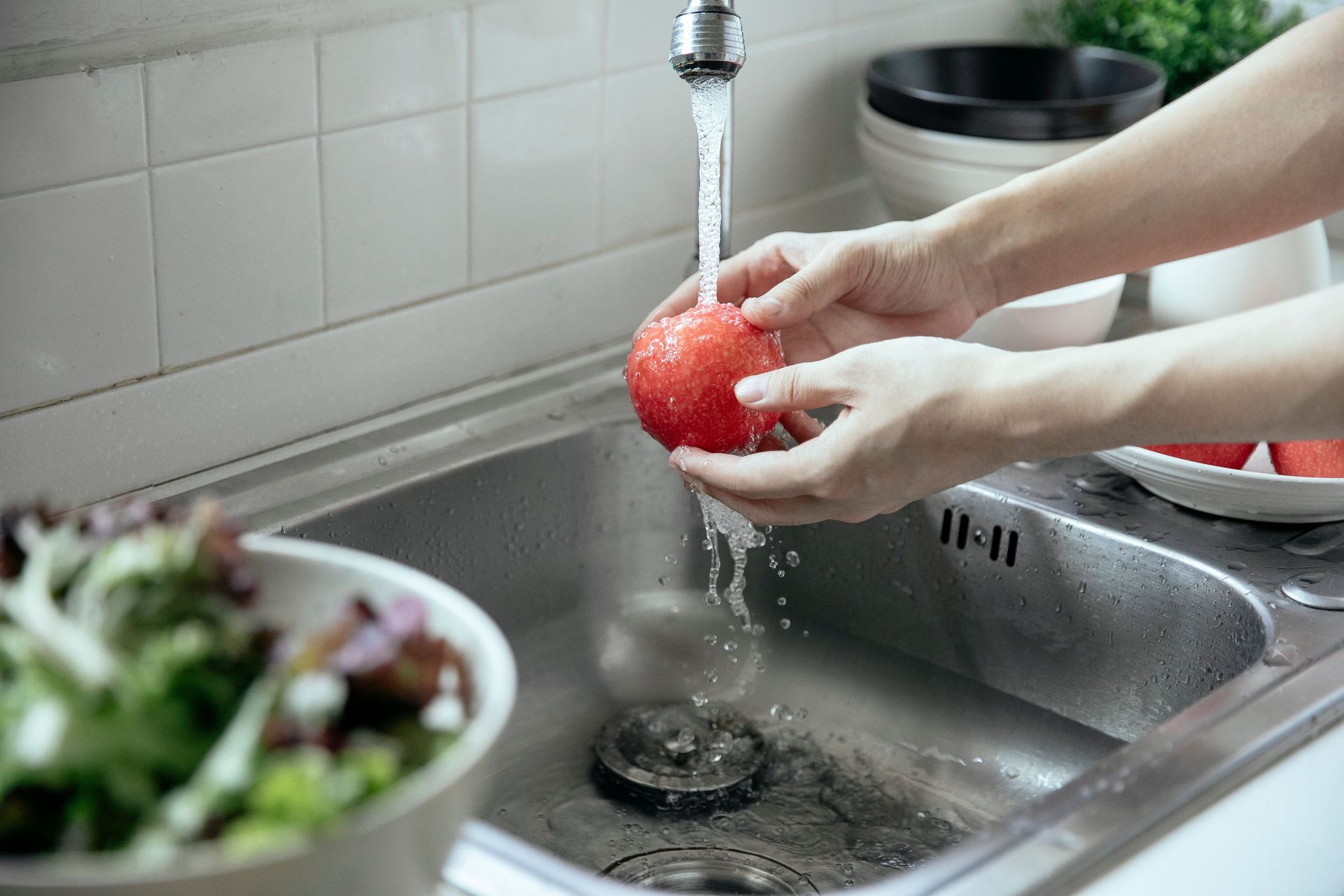 Hands washing a fresh red apple under running water at a kitchen sink.